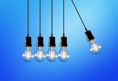 five light bulbs switched on hanging from the ceiling with one bulb swinging towards the other bulbs, on a blue background