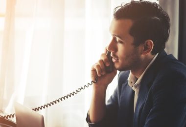 man talking on telephone whilst looking down at laptop