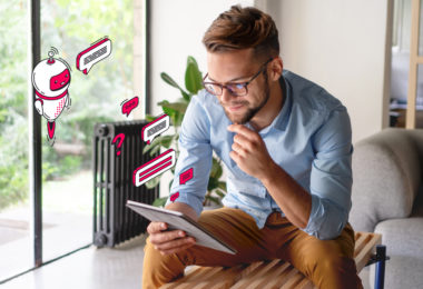 man wearing glasses sitting down and thinking whilst using tablet, chatbot and speech bubble Connect red illustrations are projected from the tablet