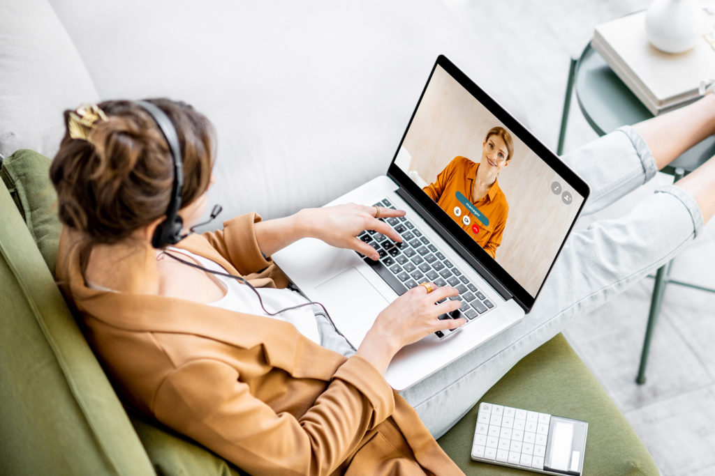 woman sitting on sofa with her feet up with headset on having a video call on her laptop and using the laptop keyboard